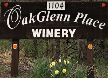 A sign for oak glenn winery with flowers in the background.